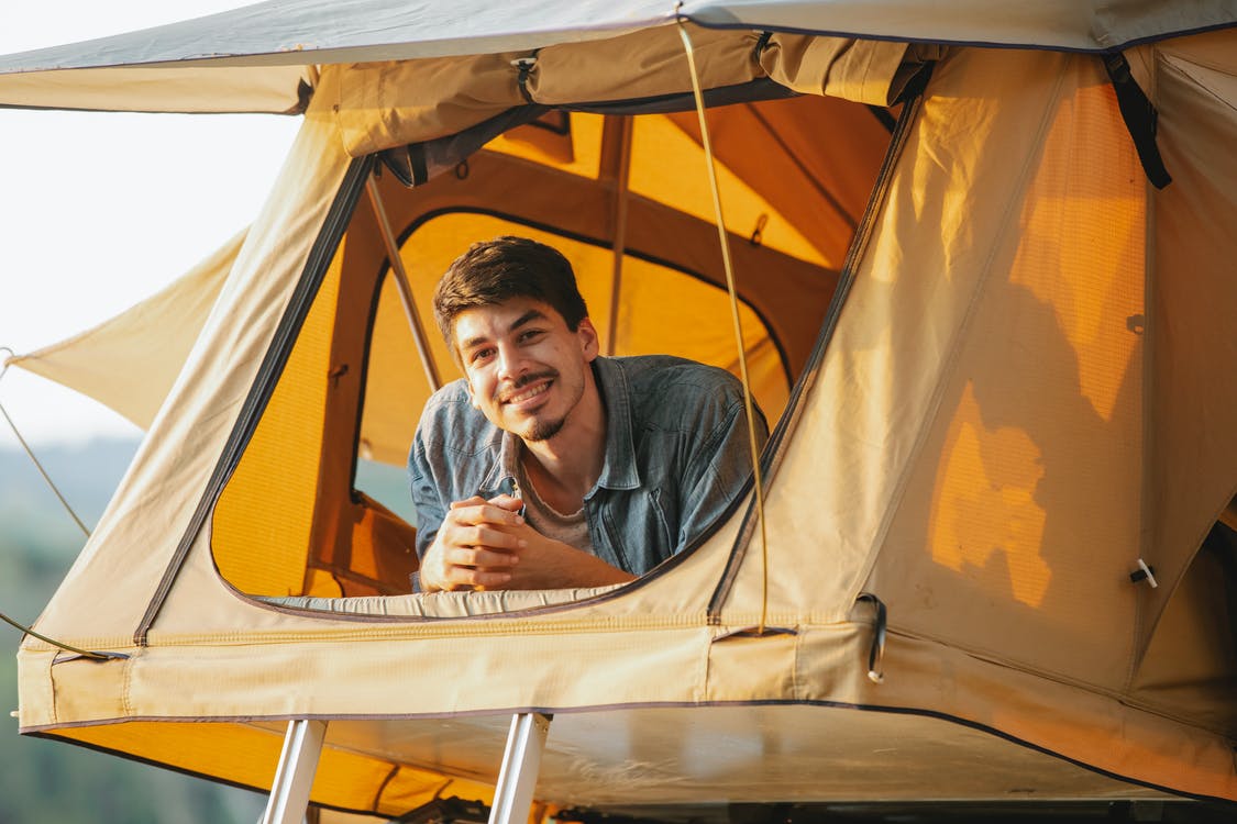 man wearing grey button-up smiling inside of canvas tent